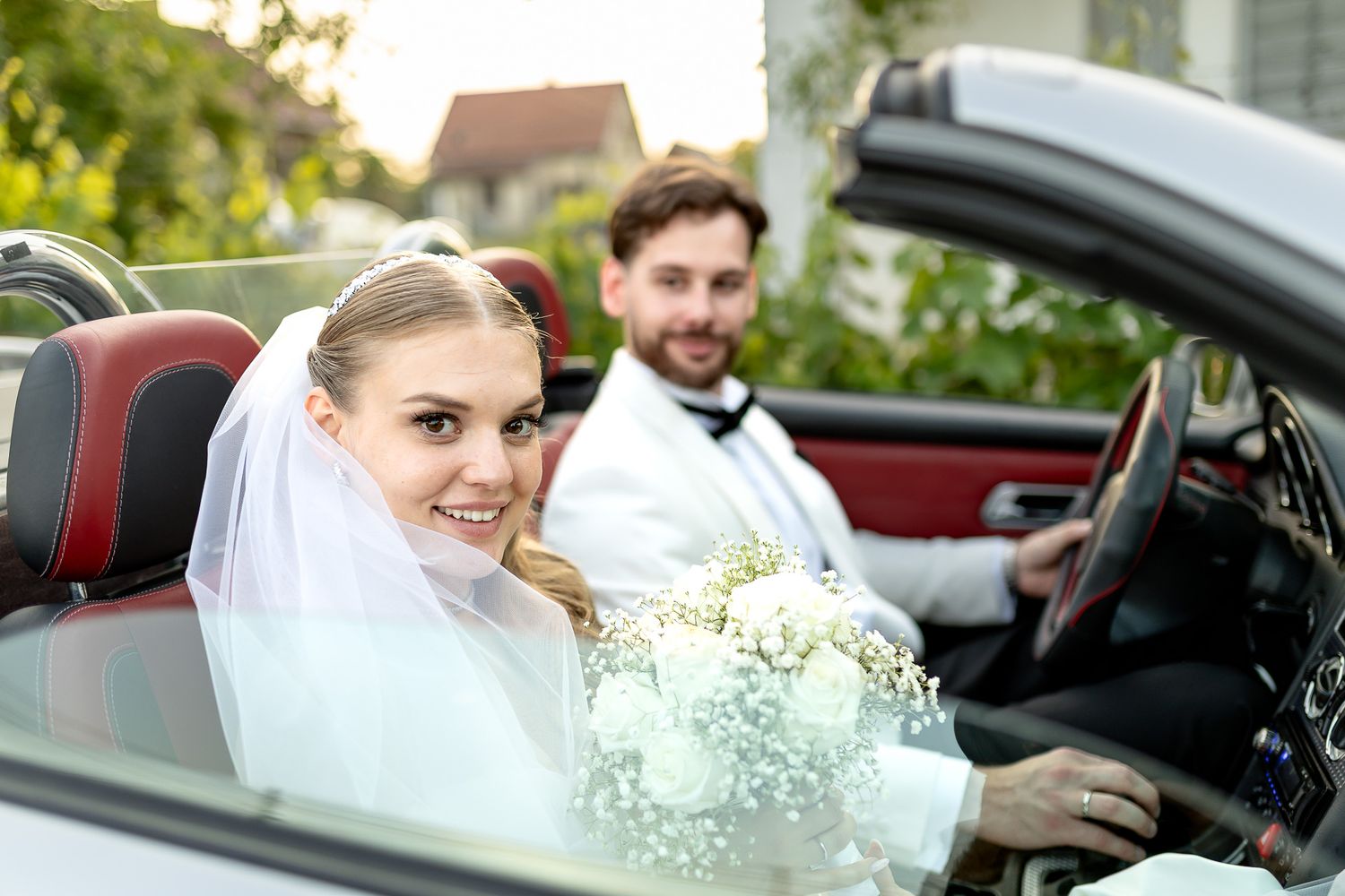 Bride and groom pose with luxury car during wedding photoshoot.