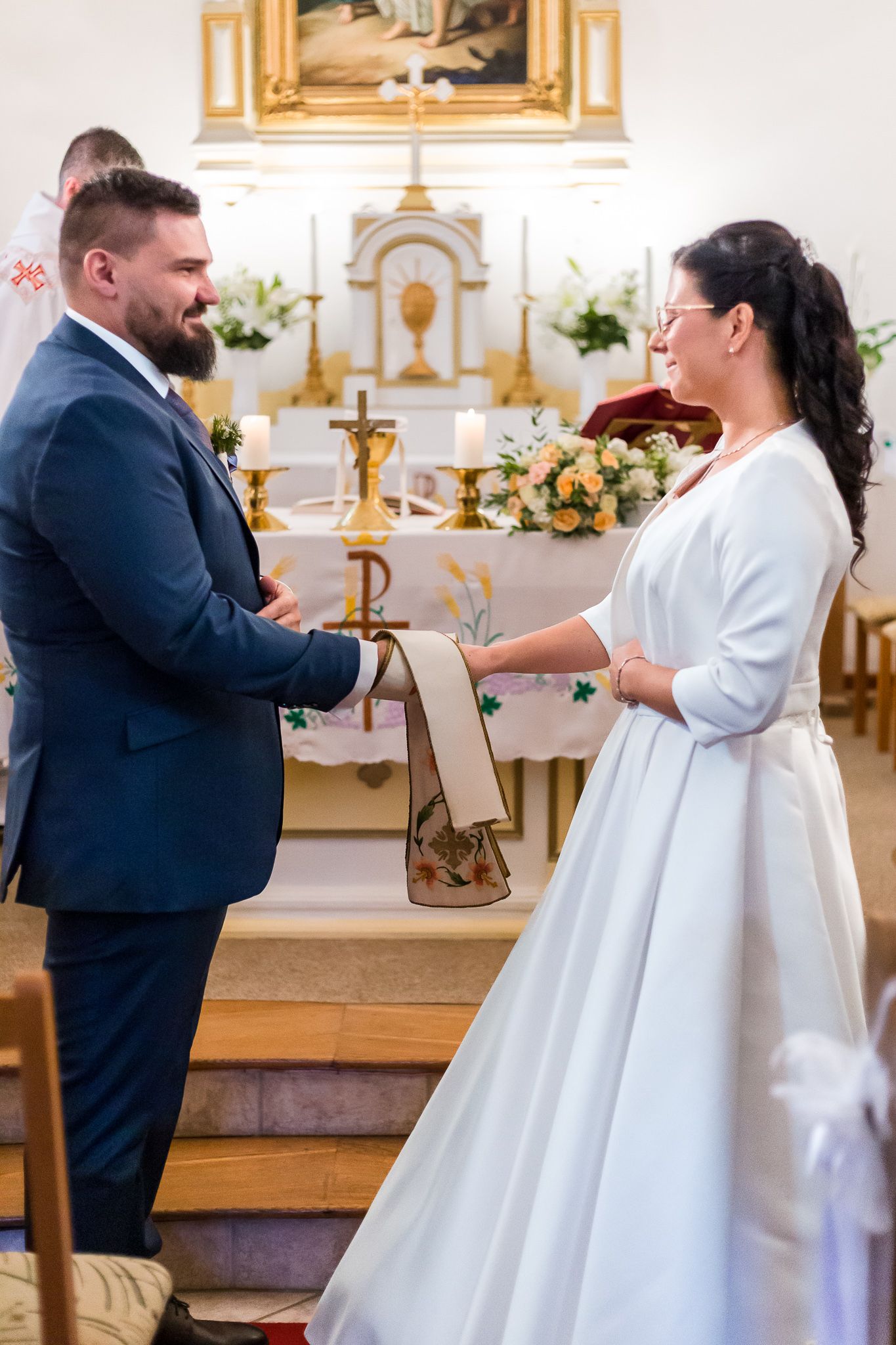A wedding ceremony takes place in a traditional church with ornate gold decor and floral arrangements on the altar.