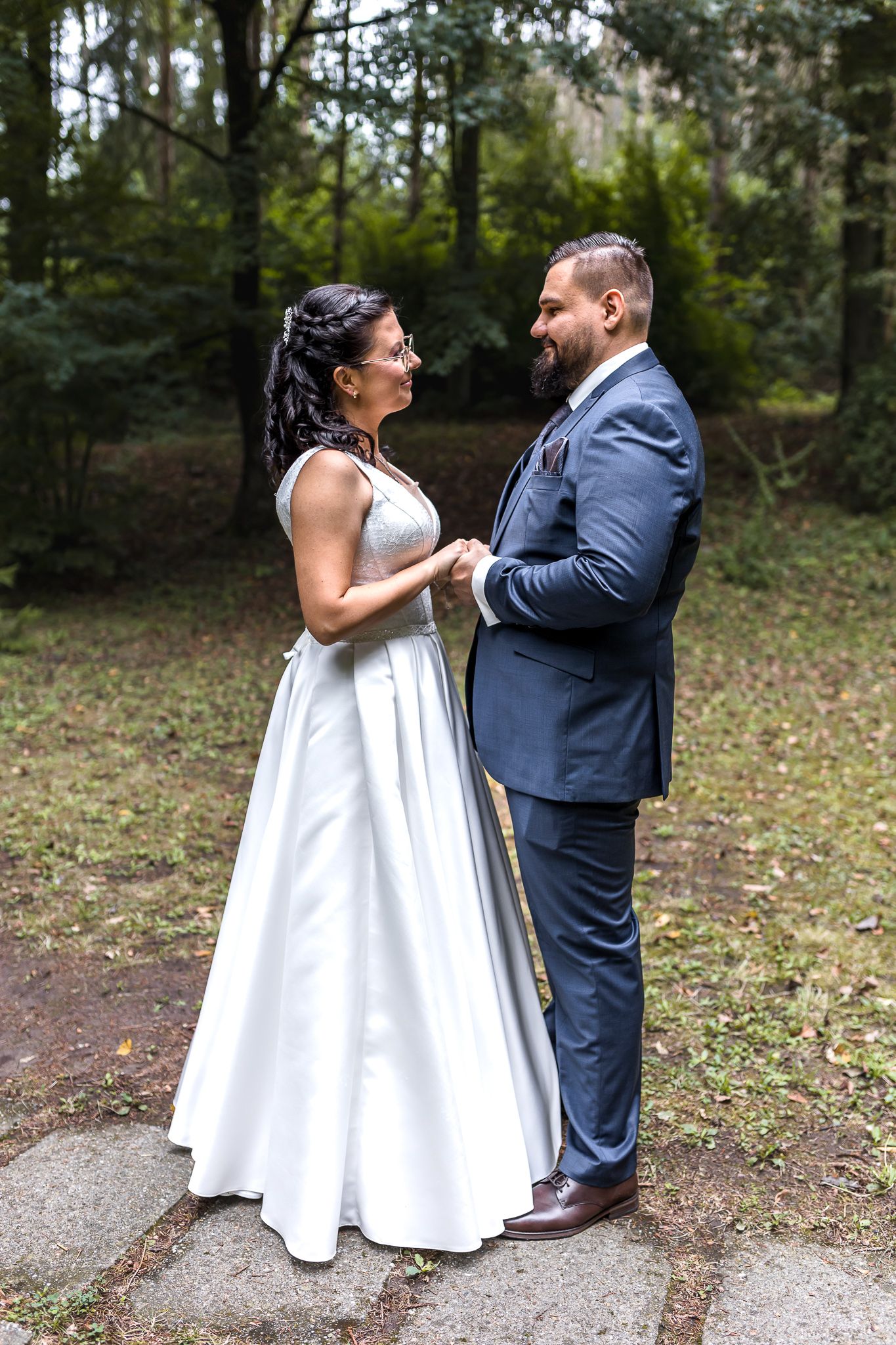 A couple in wedding attire dance together on a wooded path during their outdoor wedding celebration.