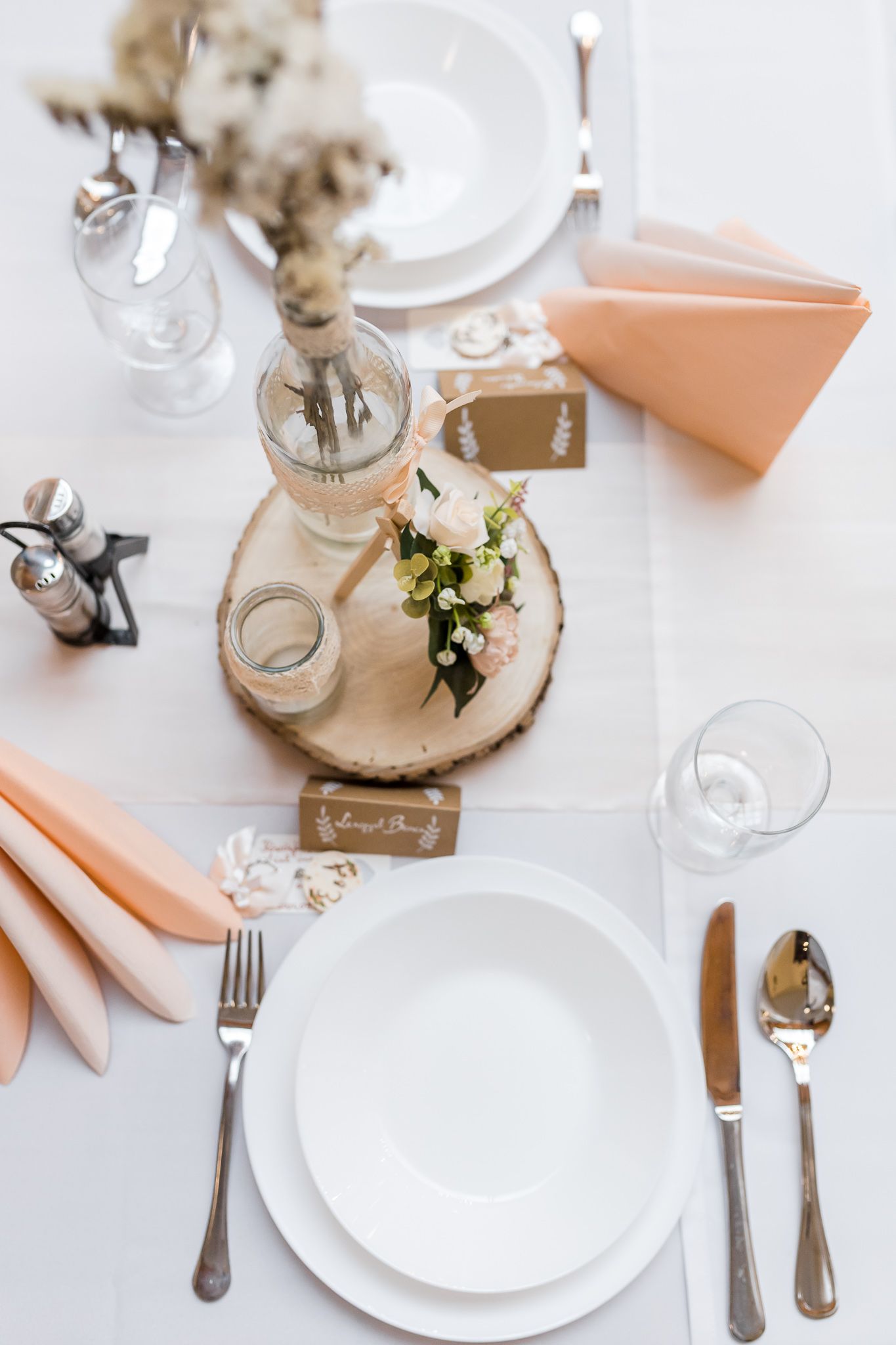 Elegant table setting with white plates, peach napkins, and rustic burlap accents for a wedding reception.