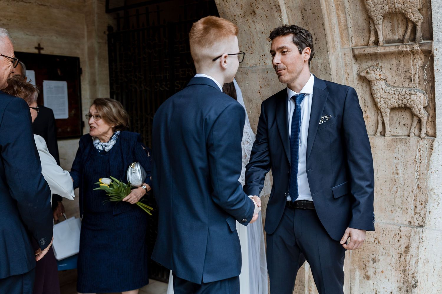 Guests in formal attire converse during an elegant event at a stone-walled venue.