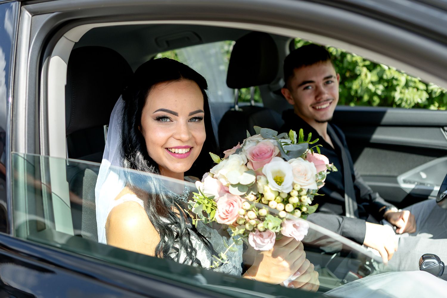 A person sits in the driver's seat of a car holding a bouquet of pink and white flowers.