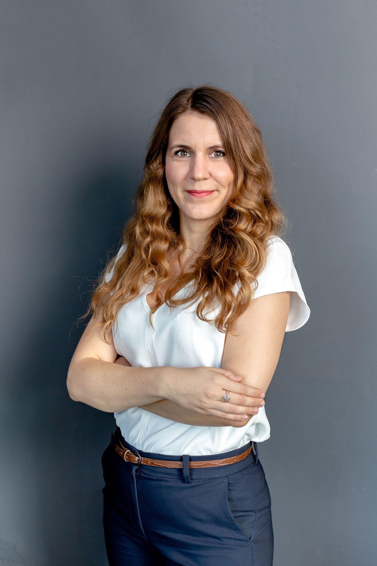 Business casual portrait with white blouse and navy trousers against grey backdrop.