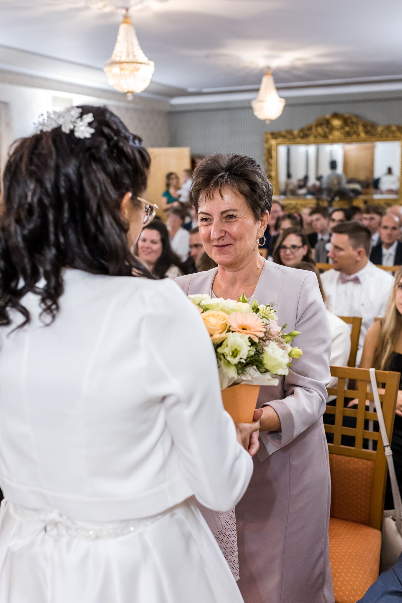 Wedding guests share joyful moments during a reception in an elegant banquet hall with crystal chandeliers.