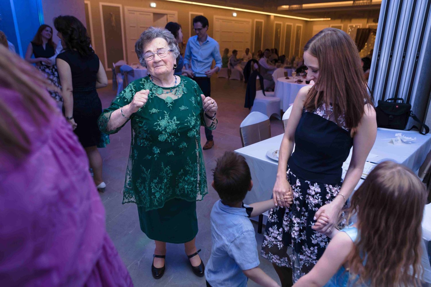 People dancing in a line at a social gathering with colorful lighting and festive atmosphere.