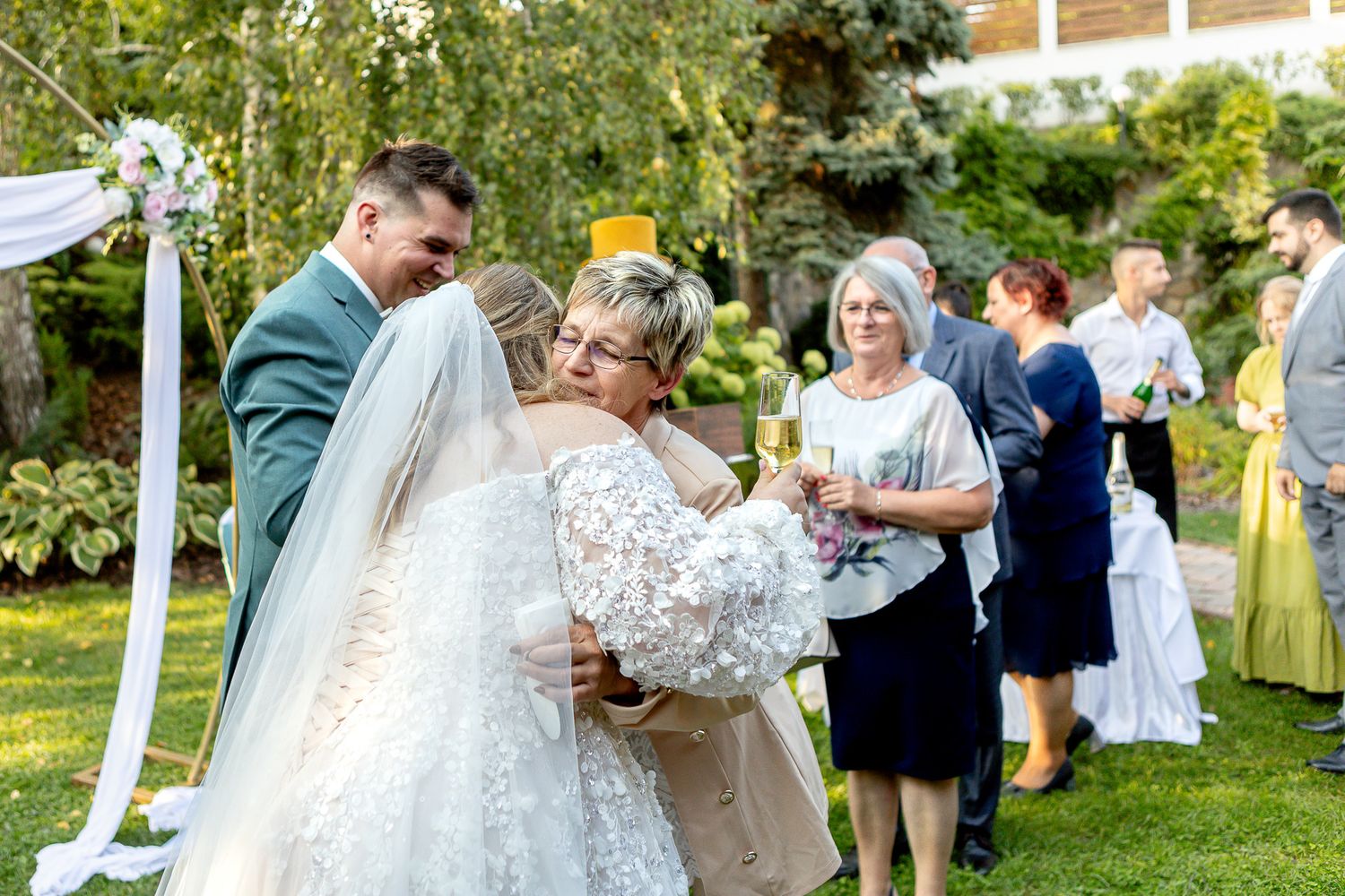 Wedding guests dance and celebrate during an outdoor garden reception under string lights and trees.