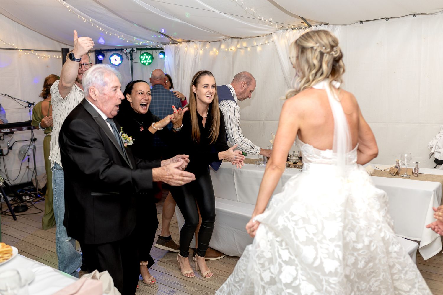 Wedding guests dance and celebrate together on the dance floor under string lights at an indoor reception.
