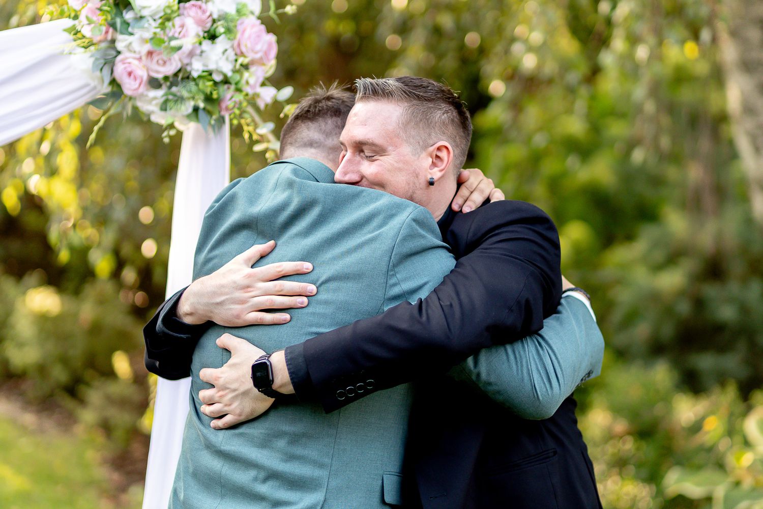 Two people embrace warmly in an outdoor setting surrounded by autumn foliage and natural light.