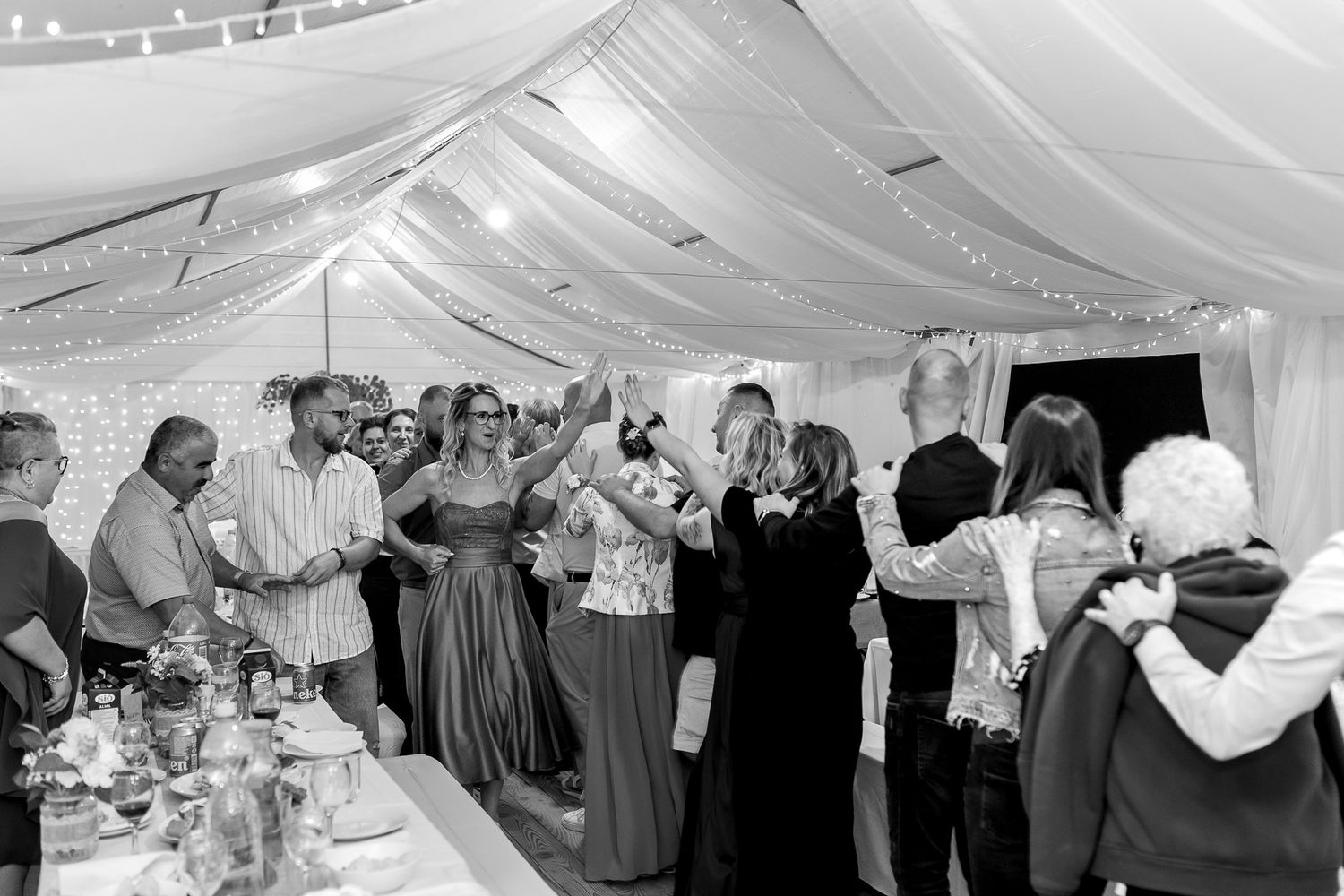 Wedding guests dance and celebrate under an elegant white tent canopy during an evening reception.