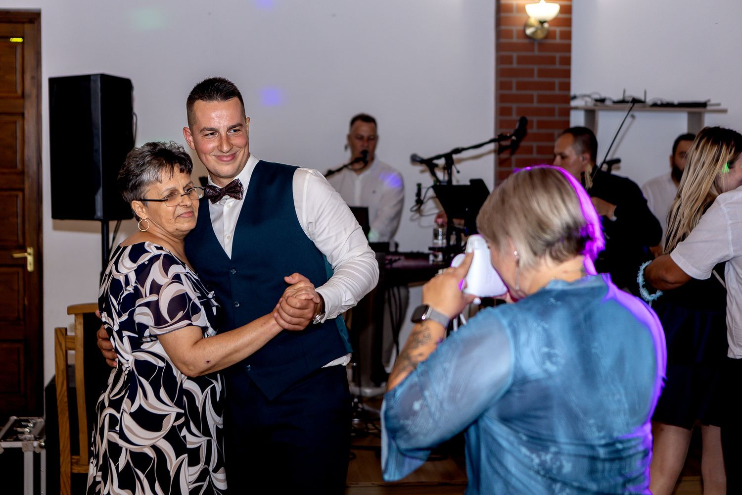 Wedding guests dancing together in a reception venue with brick walls and festive lighting.
