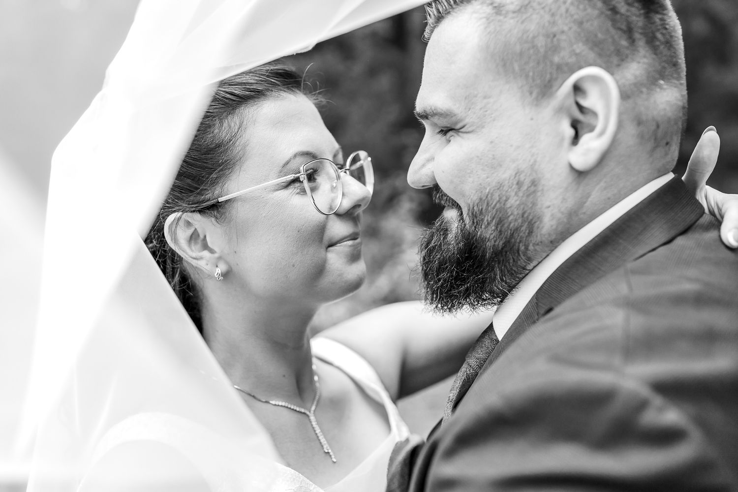 Black and white close up photo of a tender moment between a bride in glasses and bearded groom on their wedding day.