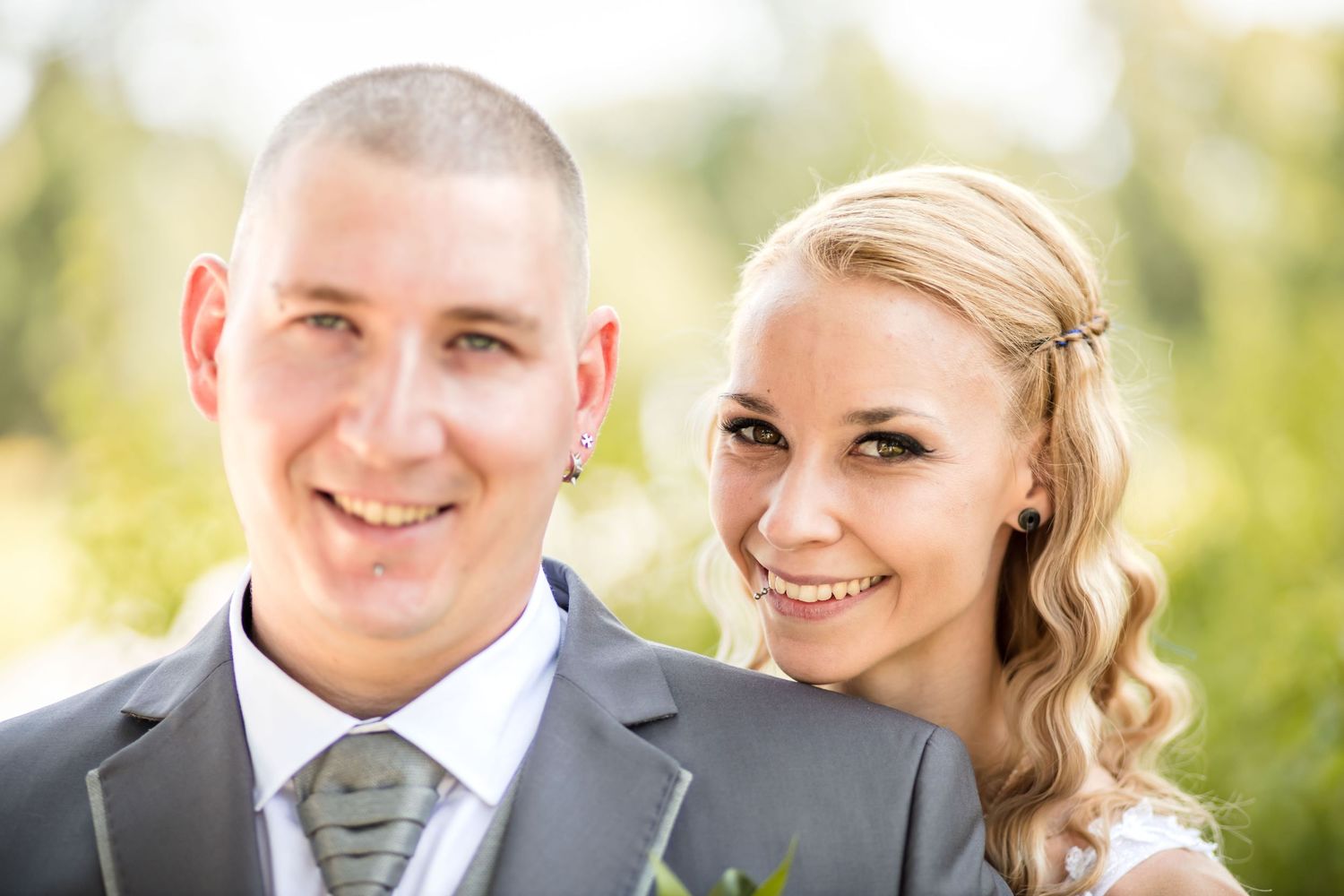 A happy couple smiles together outdoors on their wedding day wearing formal attire.