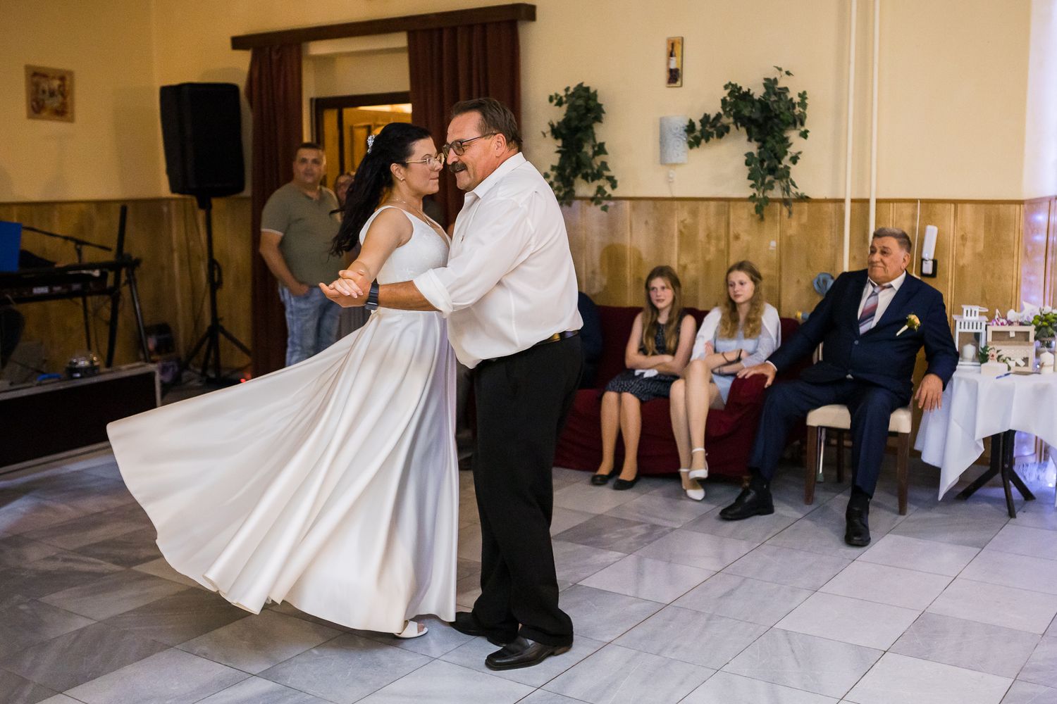 A couple shares a romantic dance dip move at a wedding reception with decorative lights in the background.
