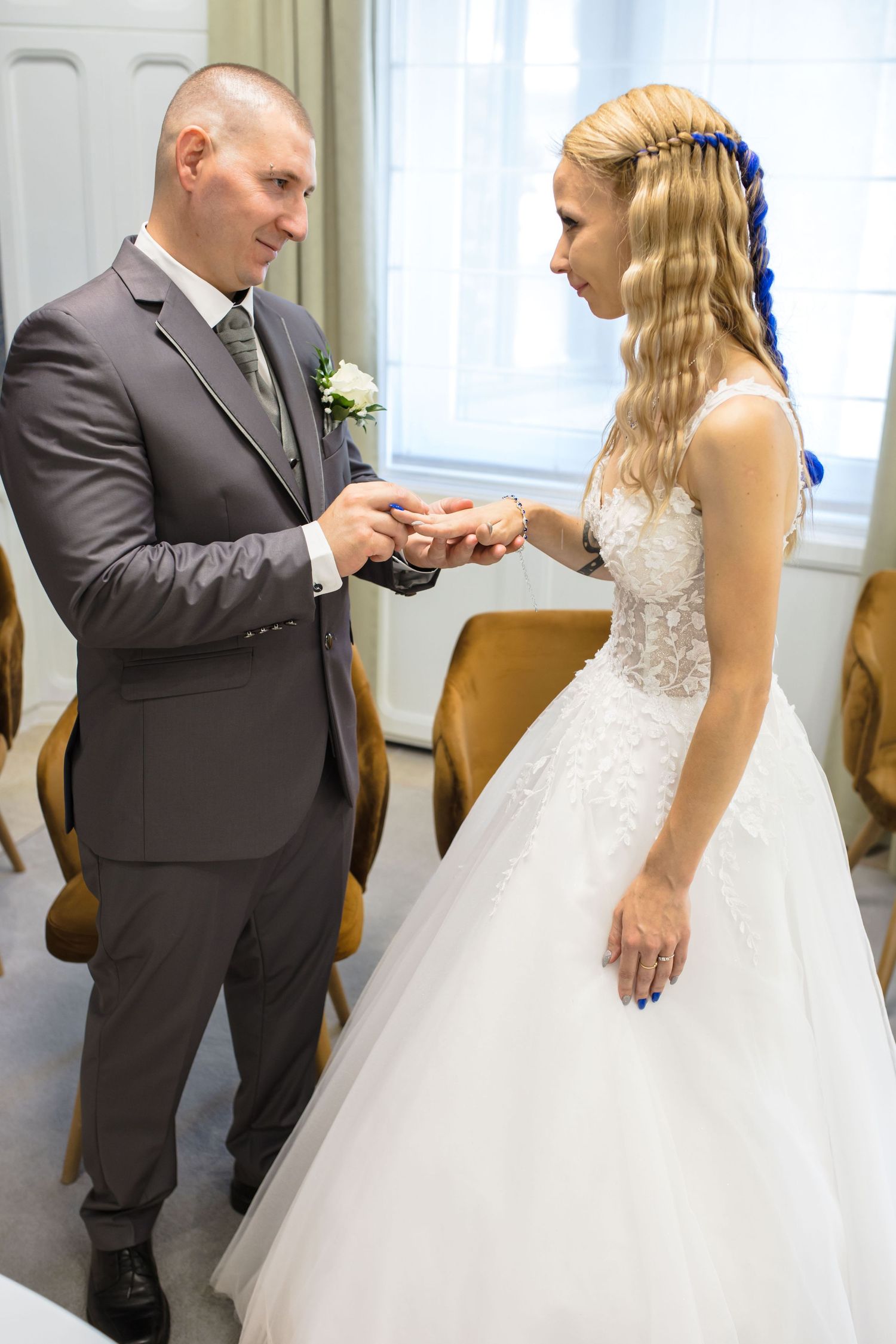 A couple shares an intimate moment during their wedding ceremony as they exchange rings in a sunlit room.