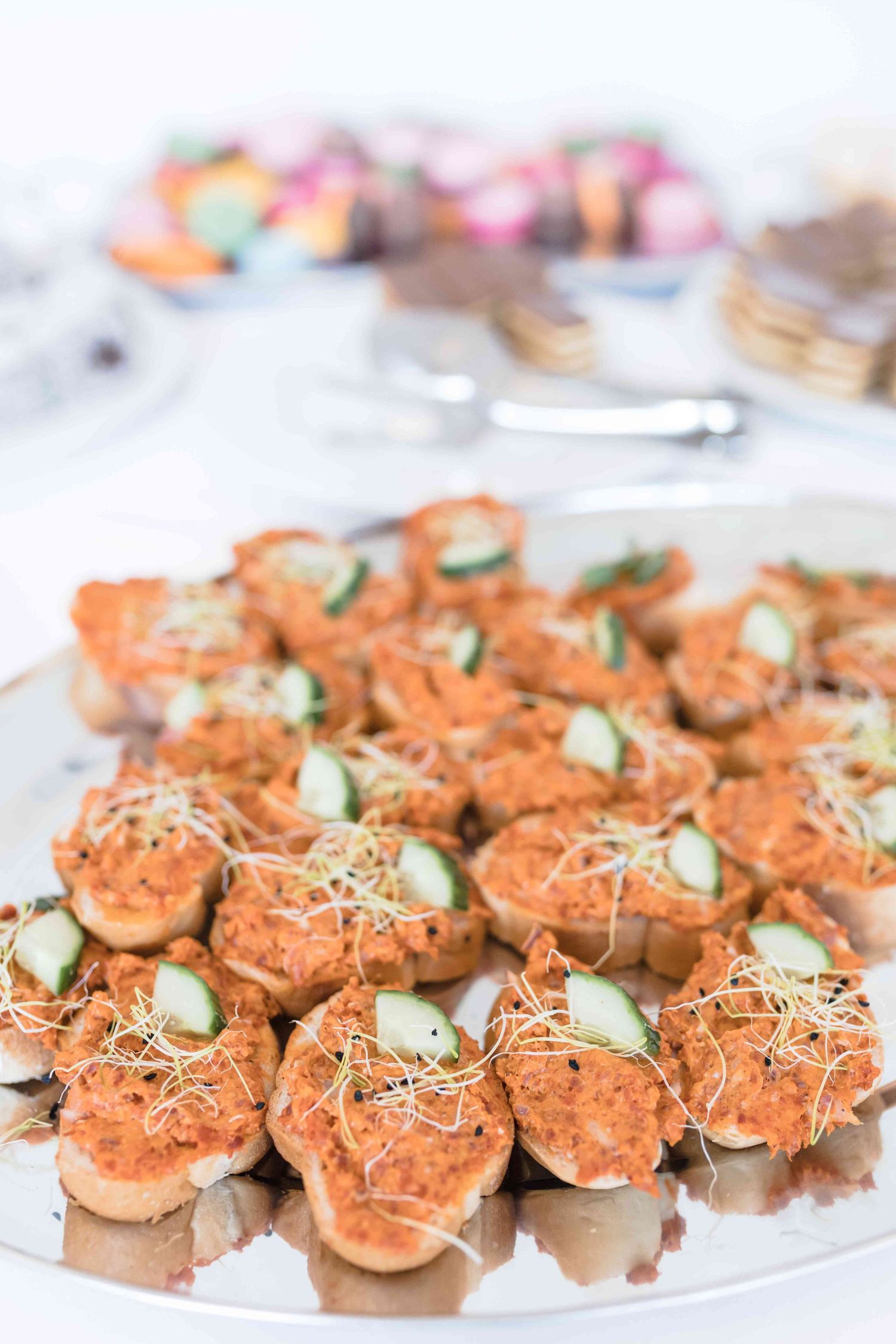 Small salmon appetizers garnished with cucumber slices and microgreens arranged on a white serving platter.