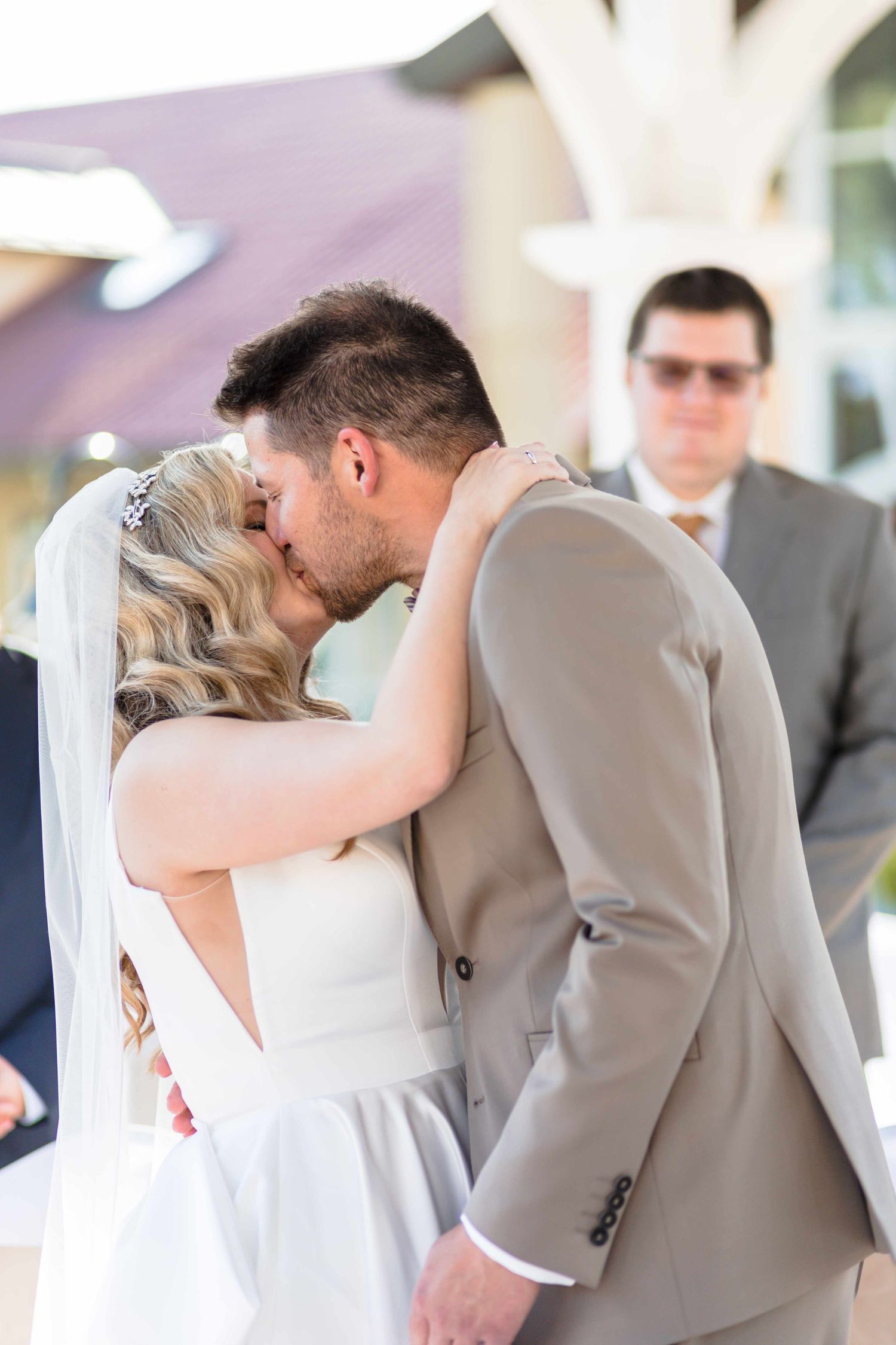 A romantic wedding couple shares a passionate kiss during their ceremony while guests look on in the background.