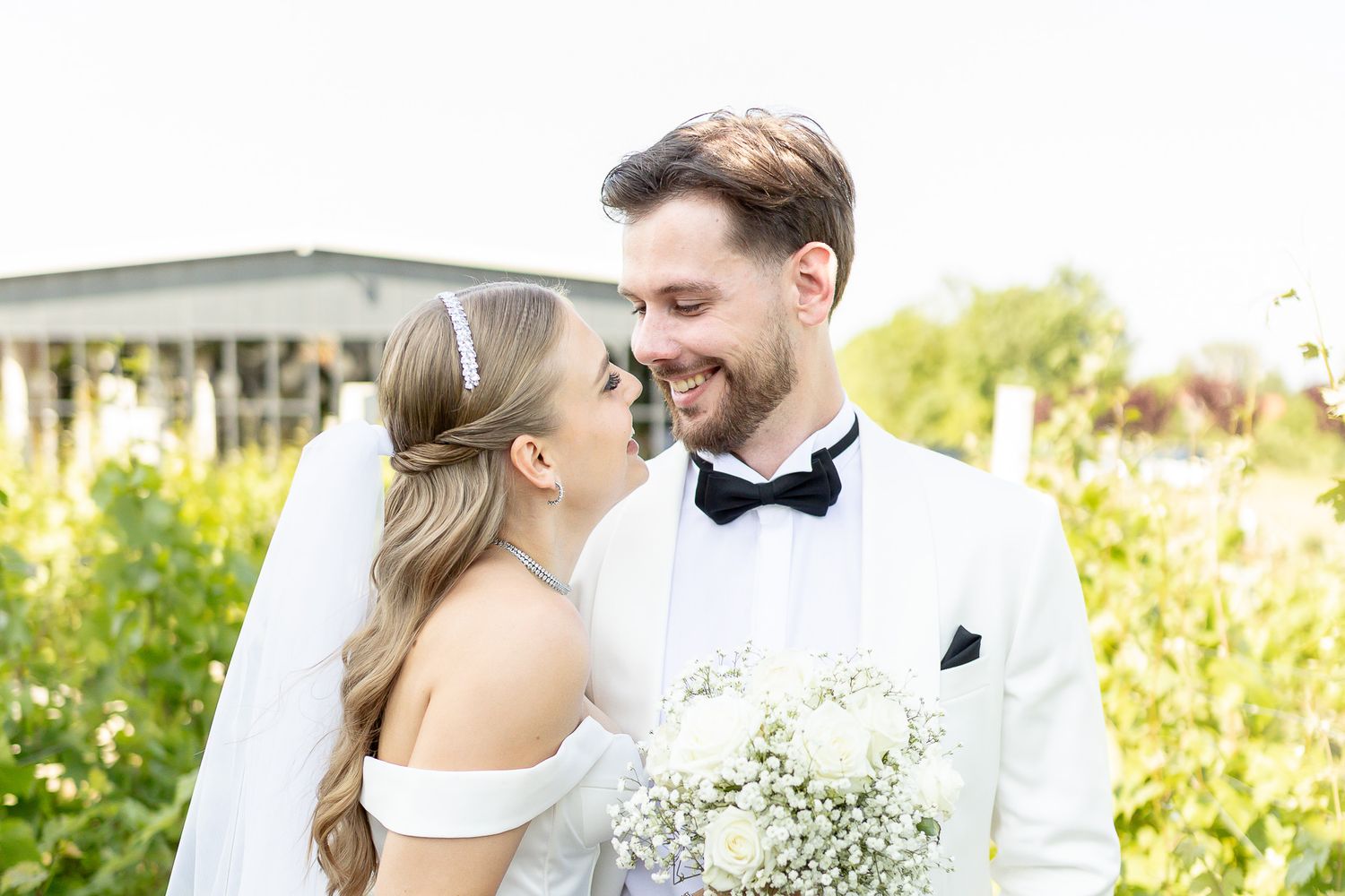 Elegant wedding couple shares intimate moments in sunlit garden setting.