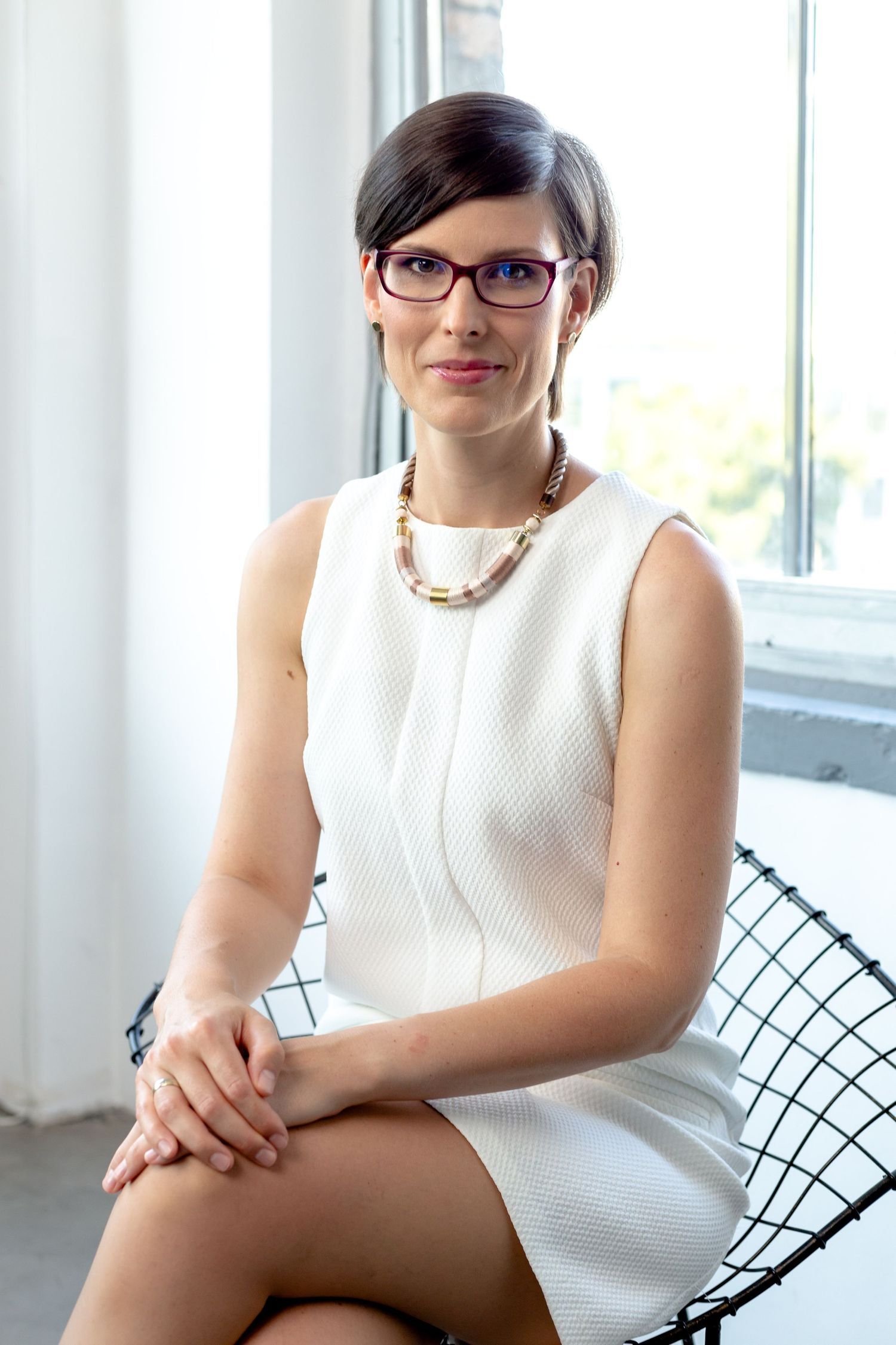 Modern business portrait in bright studio with wire chair and white sleeveless outfit.