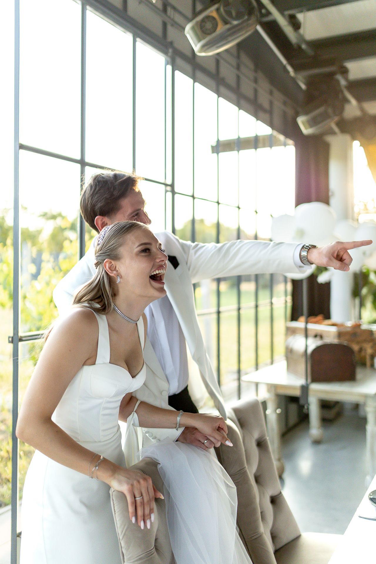 Wedding celebration with guests dancing energetically in a bright venue with large windows.