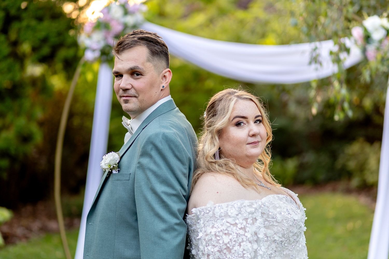 A couple shares a romantic moment under white drapery during their outdoor garden wedding.