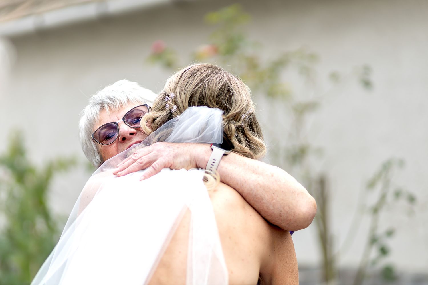 A couple embraces in an intimate moment outdoors with greenery visible in the background.