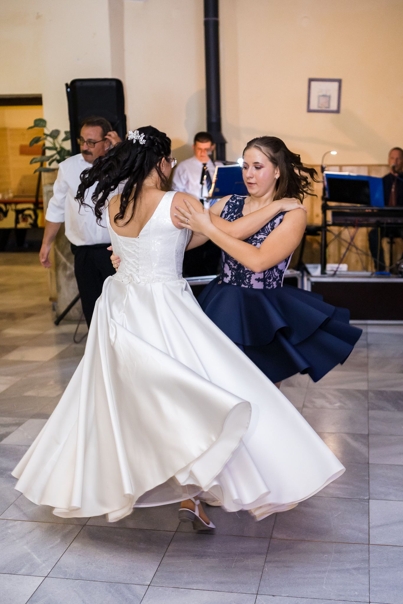 Two dancers in navy blue and white dresses perform a synchronized dip move on a dance floor during a performance.