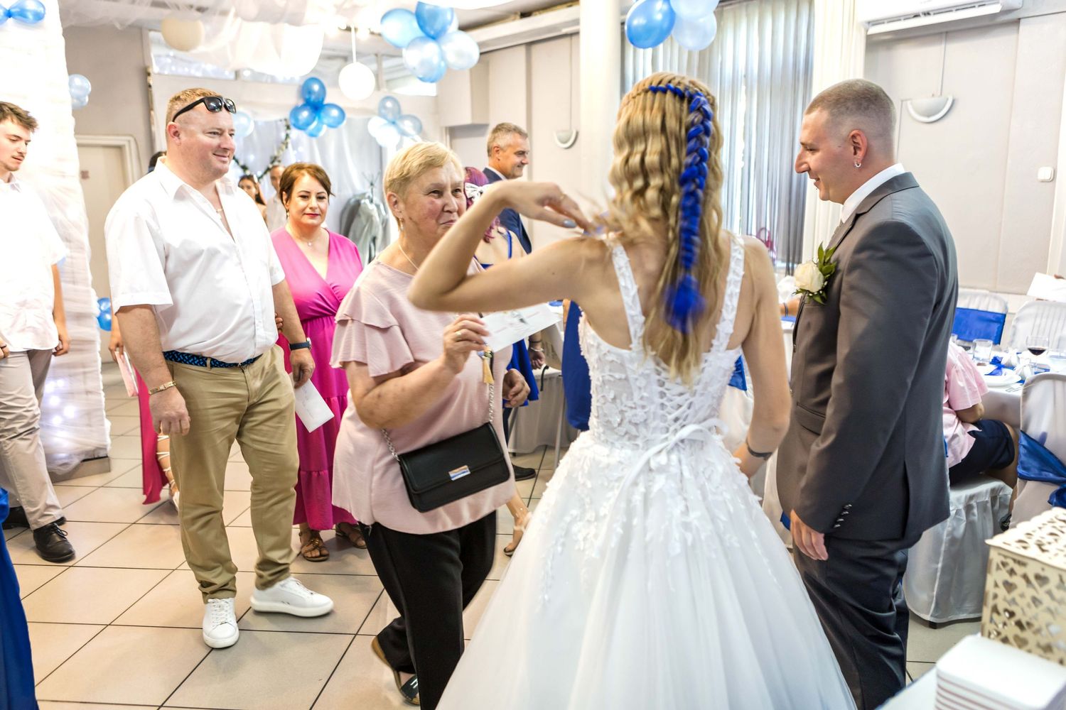 People dancing and celebrating at a wedding reception with blue balloon decorations in the background.