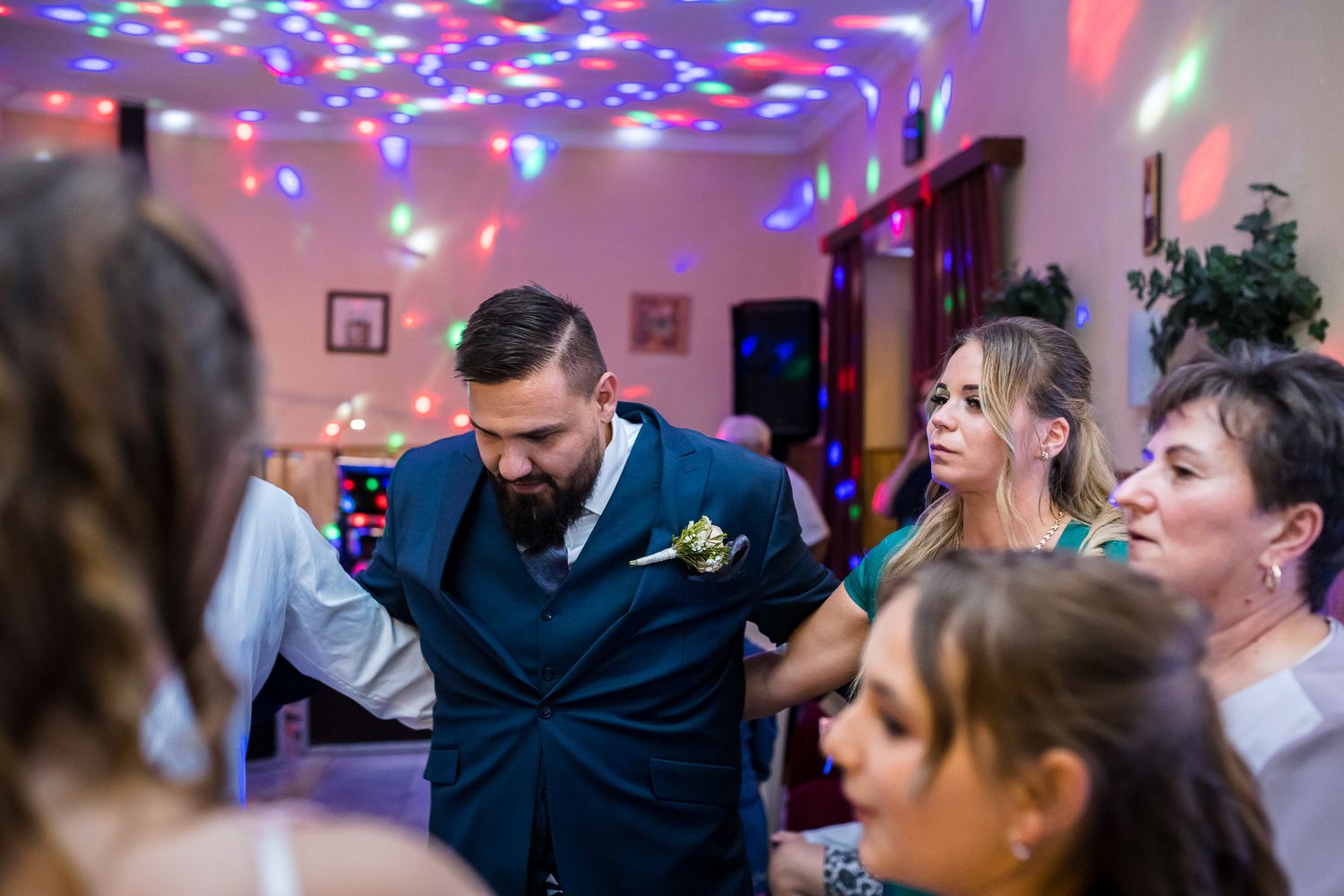 Wedding guests dance and celebrate on a colorful dance floor illuminated by vibrant disco lights during a reception party.