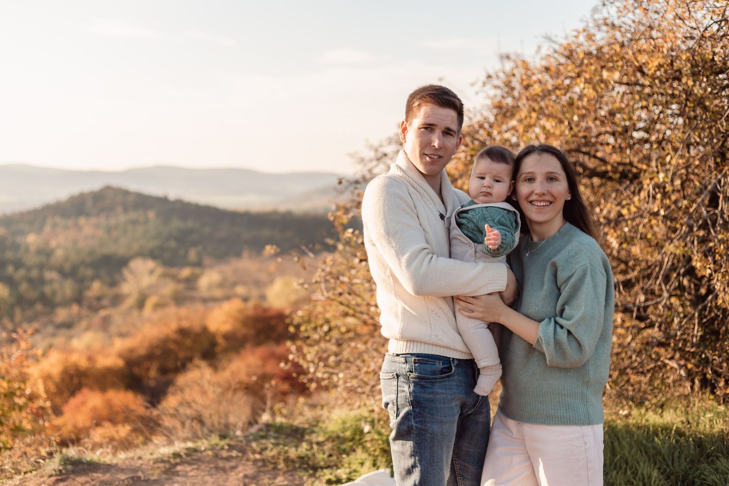 Family photoshoot in autumn setting with golden mountain landscape.