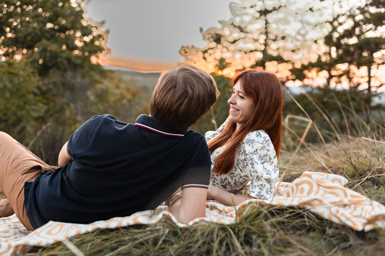 Couple relaxing together on a blanket during sunset in a natural outdoor setting.