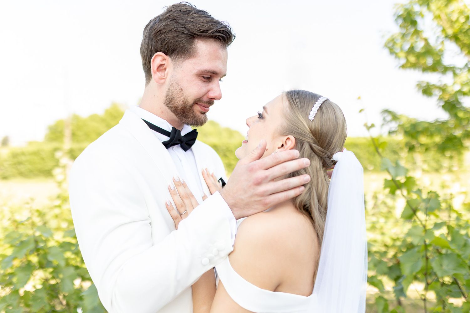 Wedding couple shares tender moments against a bright outdoor backdrop.
