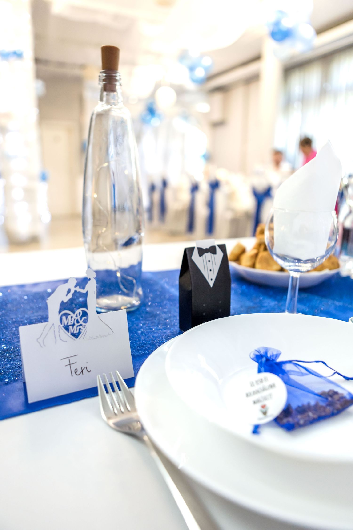 White place settings with blue table runners and wine bottles create an elegant wedding reception table decor arrangement.