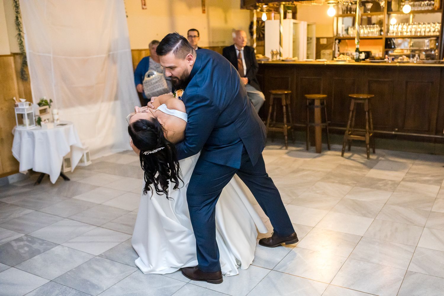 A romantic couple in formal attire dips gracefully during their first dance at an elegant wedding reception.