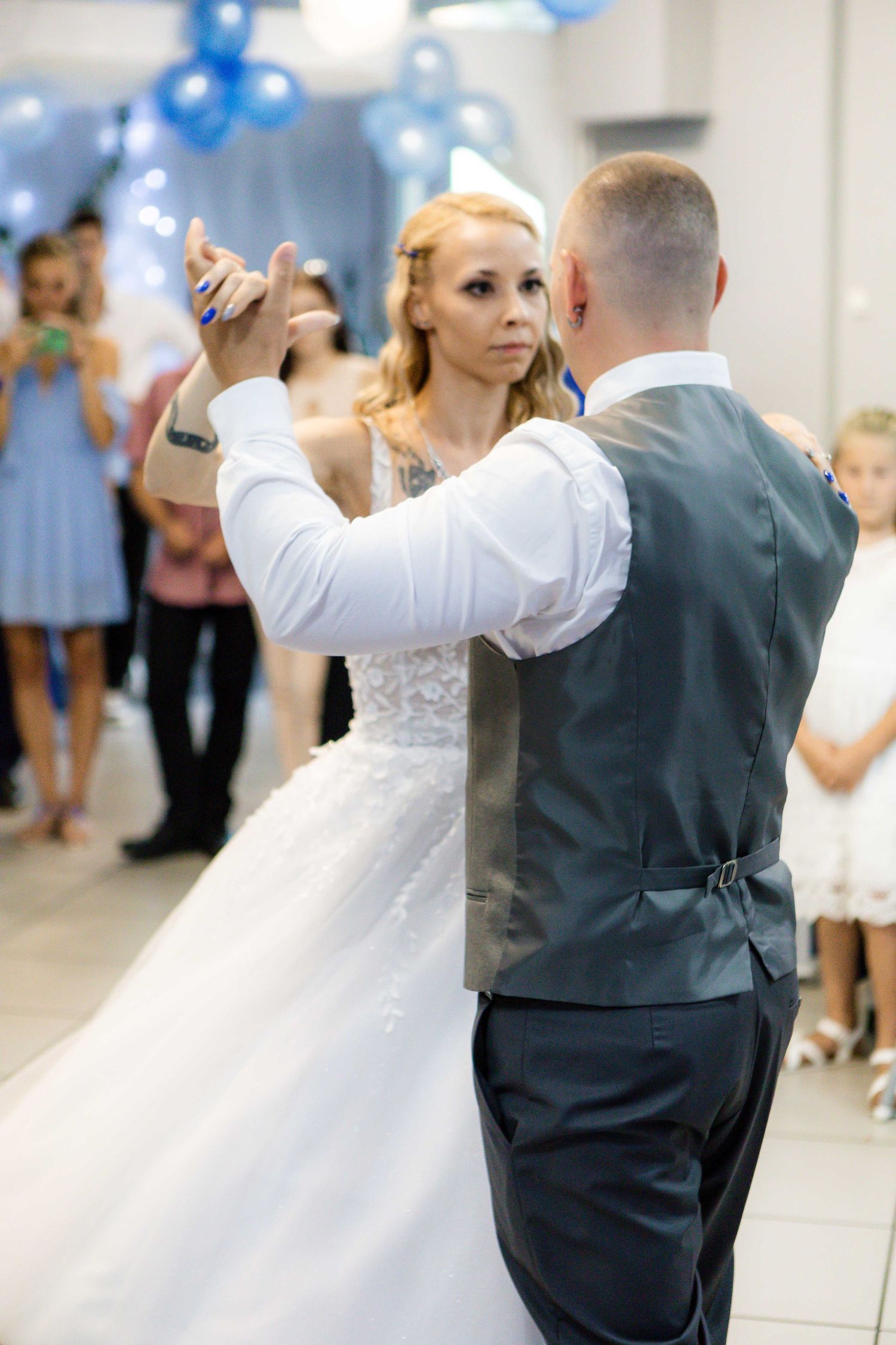 A couple performs an elegant dance at their wedding reception with blue balloons decorating the venue.