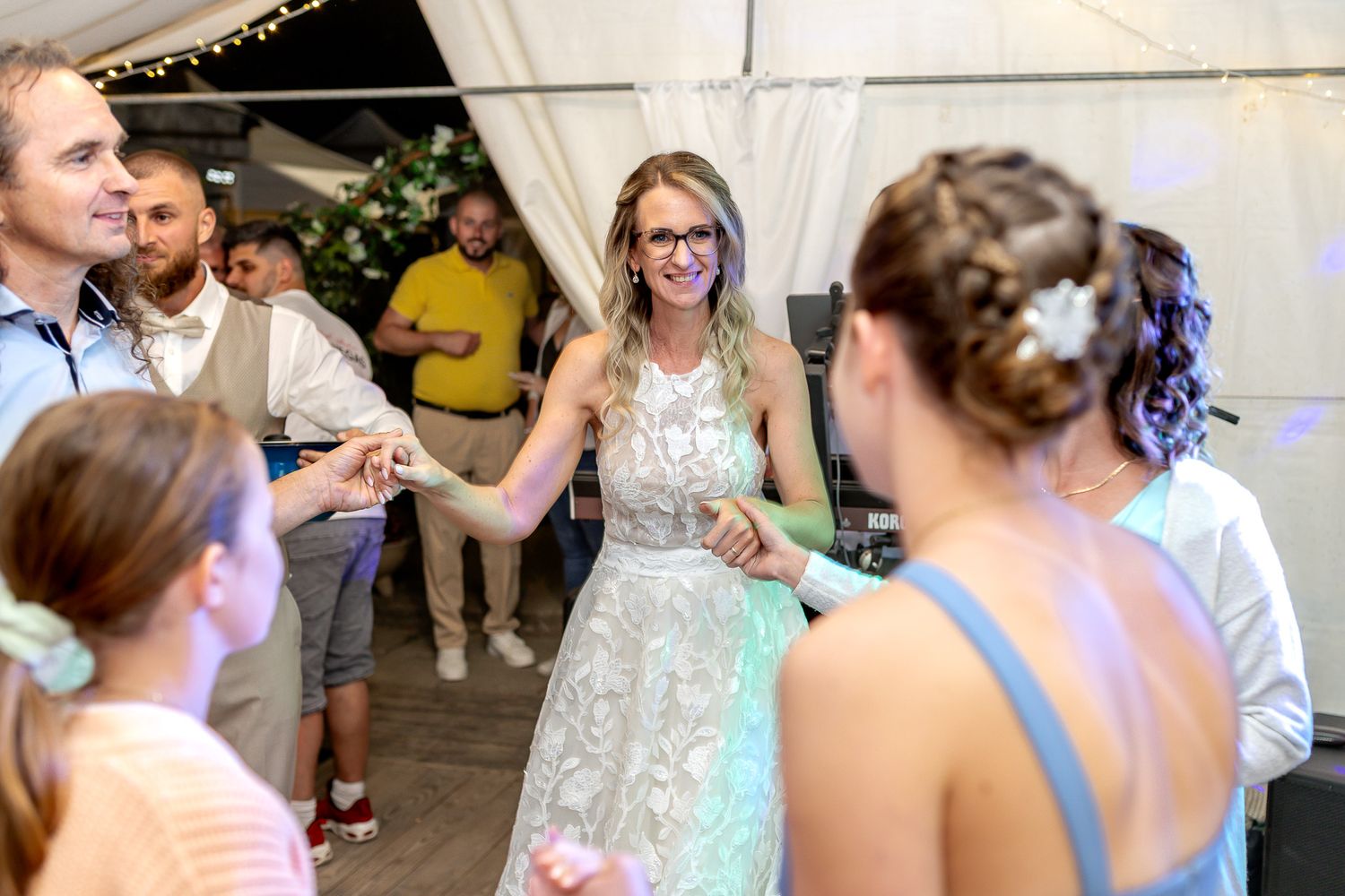 Wedding guests dancing together in a reception hall decorated with string lights and elegant decor.