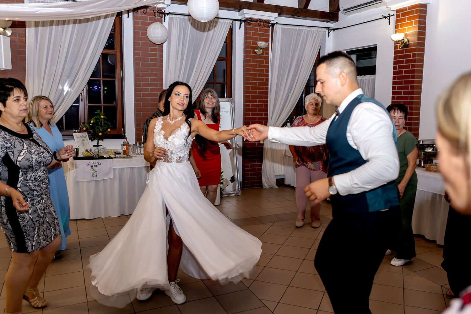 Couples dancing together at a wedding reception in a brick-walled venue decorated with white curtains and lighting.