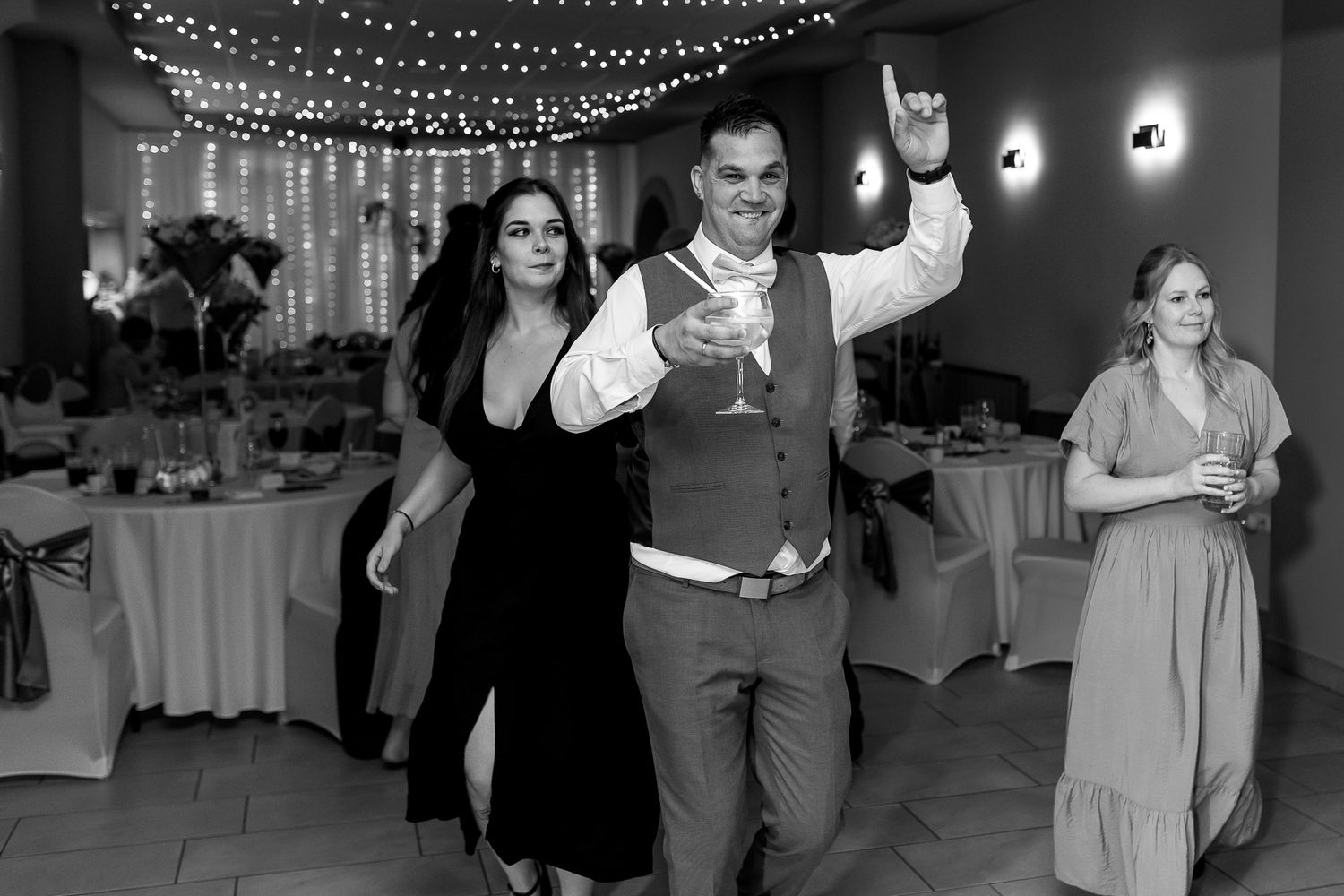 Wedding guests dance and celebrate on a dimly lit dance floor decorated with string lights overhead.