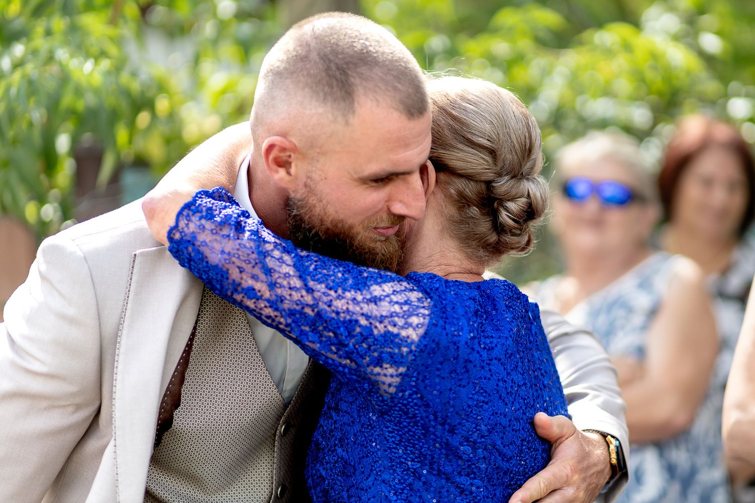 Wedding party in gray suits and royal blue dresses gathered outdoors during a celebration.