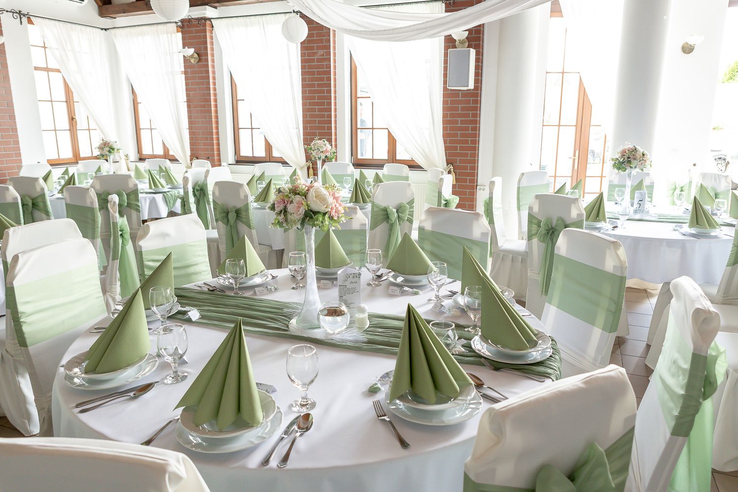 Wedding reception tables decorated in sage green and white with elegant place settings and floral centerpieces.
