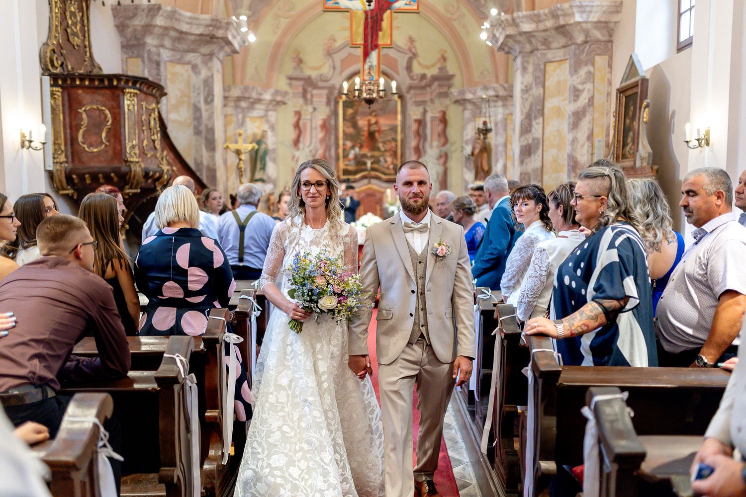 Wedding ceremony taking place in an ornate church with guests watching as the couple exchanges vows at the altar.