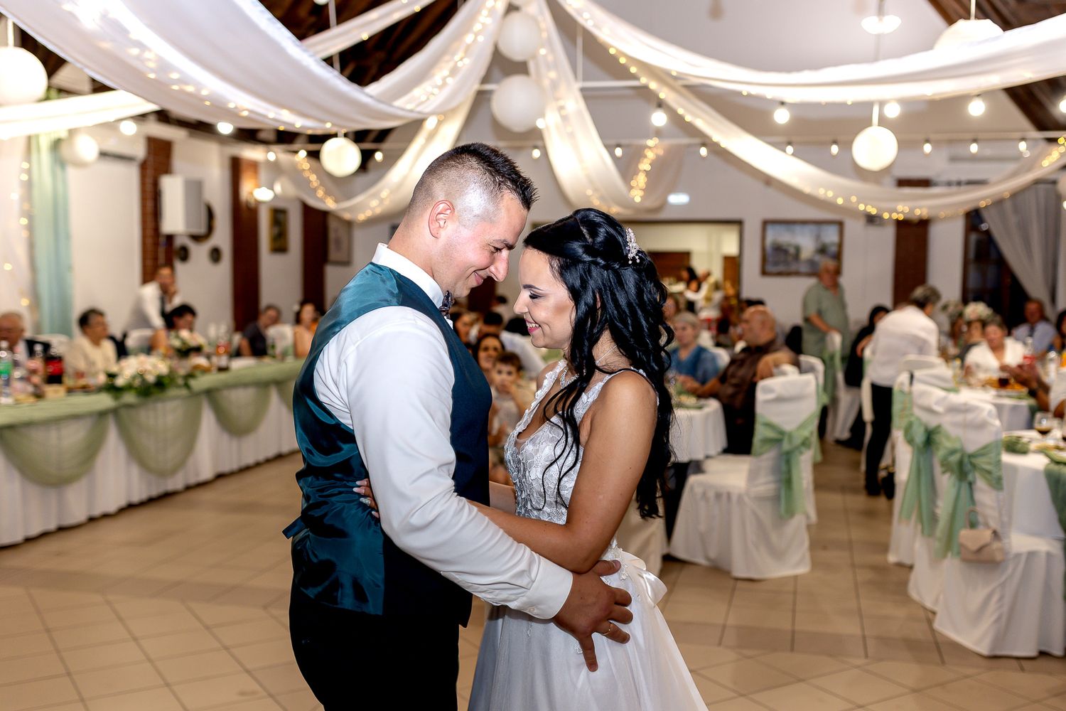 A couple shares an intimate dance moment at their wedding reception under white draped decor and soft lighting.