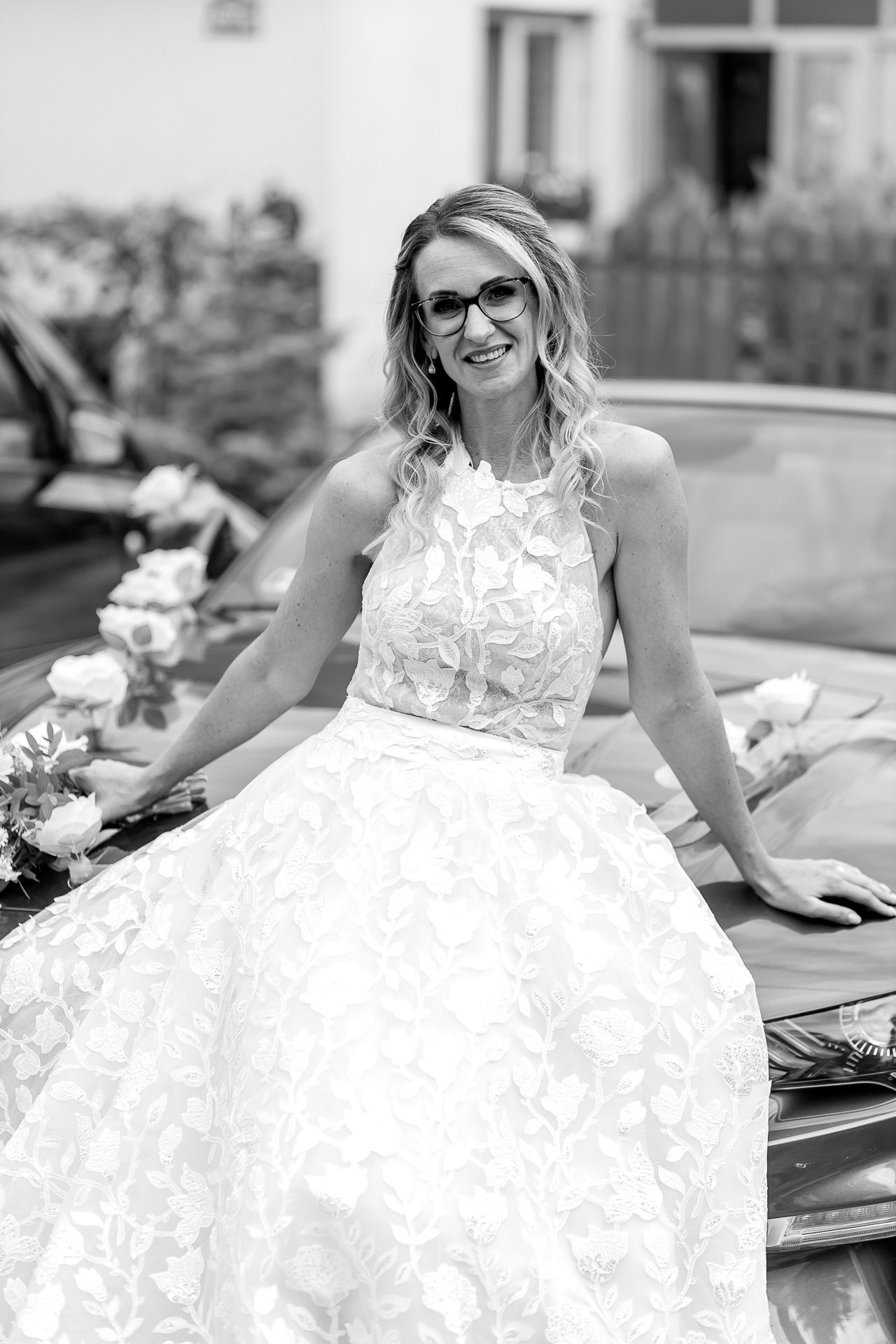 A bride in a white lace wedding dress smiles while sitting outdoors during a photo session.