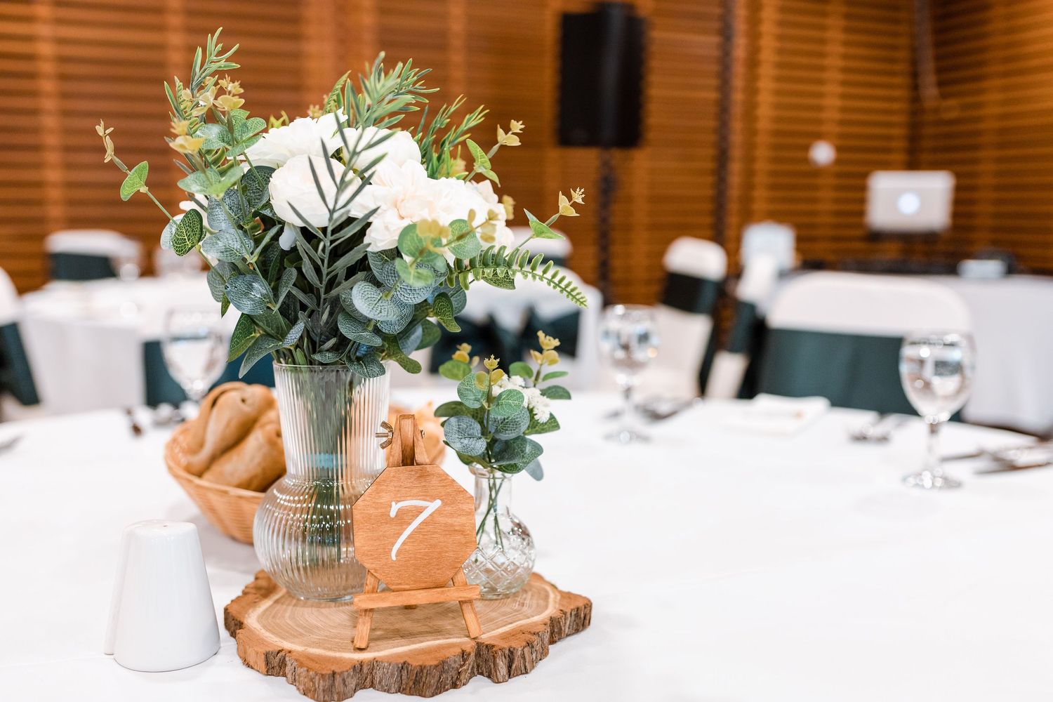 Rustic wedding reception table settings with wooden log centerpieces, eucalyptus greenery, and white table linens.