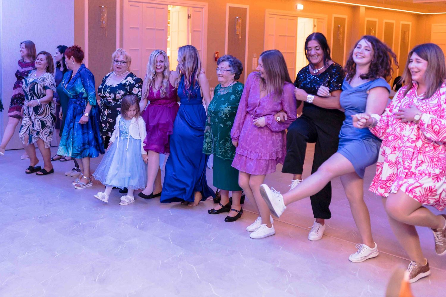 Wedding guests dance in a line at a reception while following choreographed steps on a glowing dance floor.