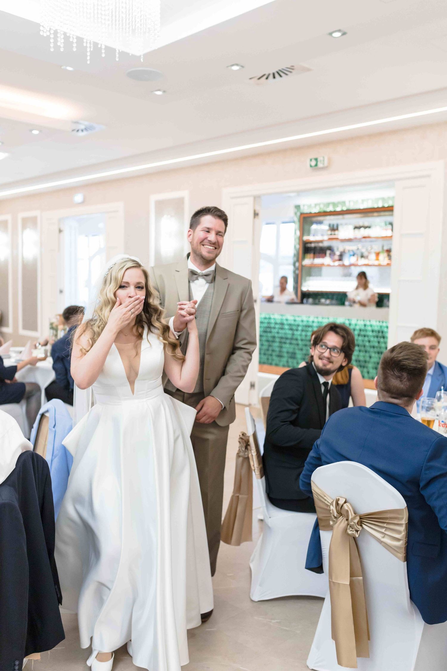 Wedding guests celebrate and dance together in a bright reception venue with white chair covers and decor.