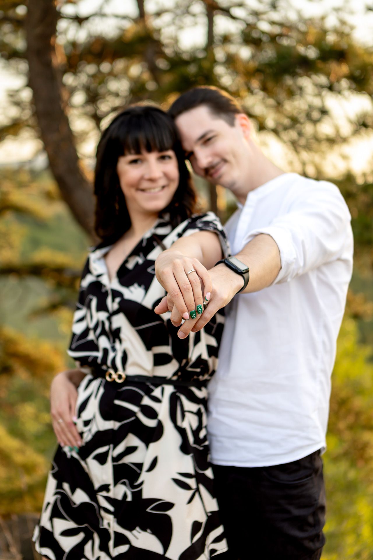 A couple in black and white clothing poses playfully against a natural outdoor backdrop.