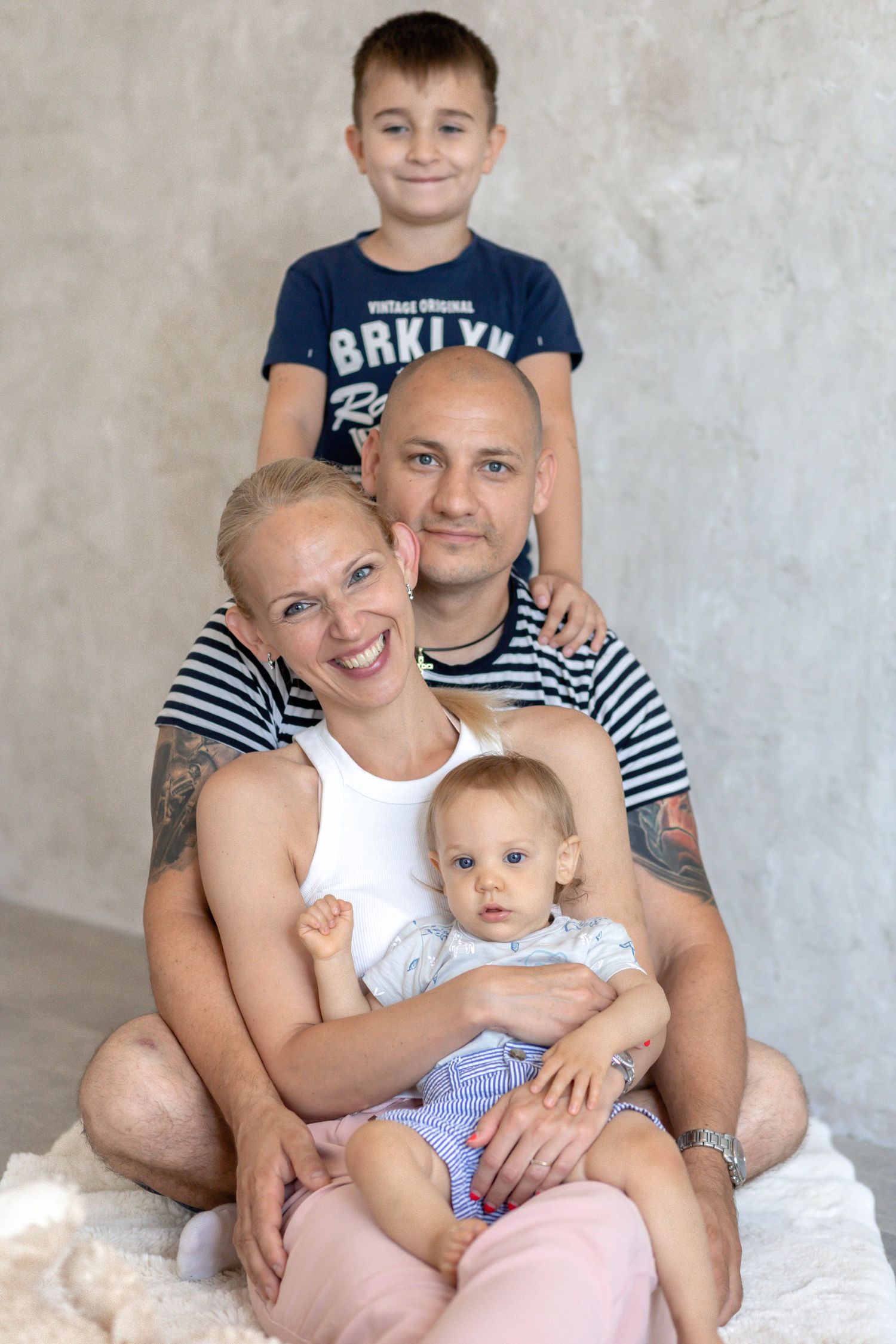 Indoor family photoshoot with striped and navy outfits against neutral wall.