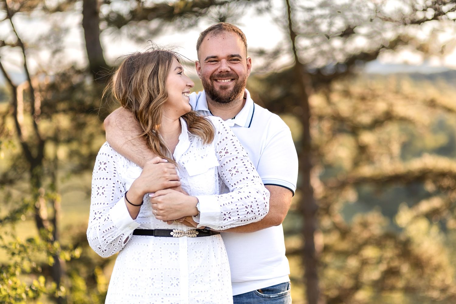 Couple shares intimate moments in white outfits against natural mountain backdrop.