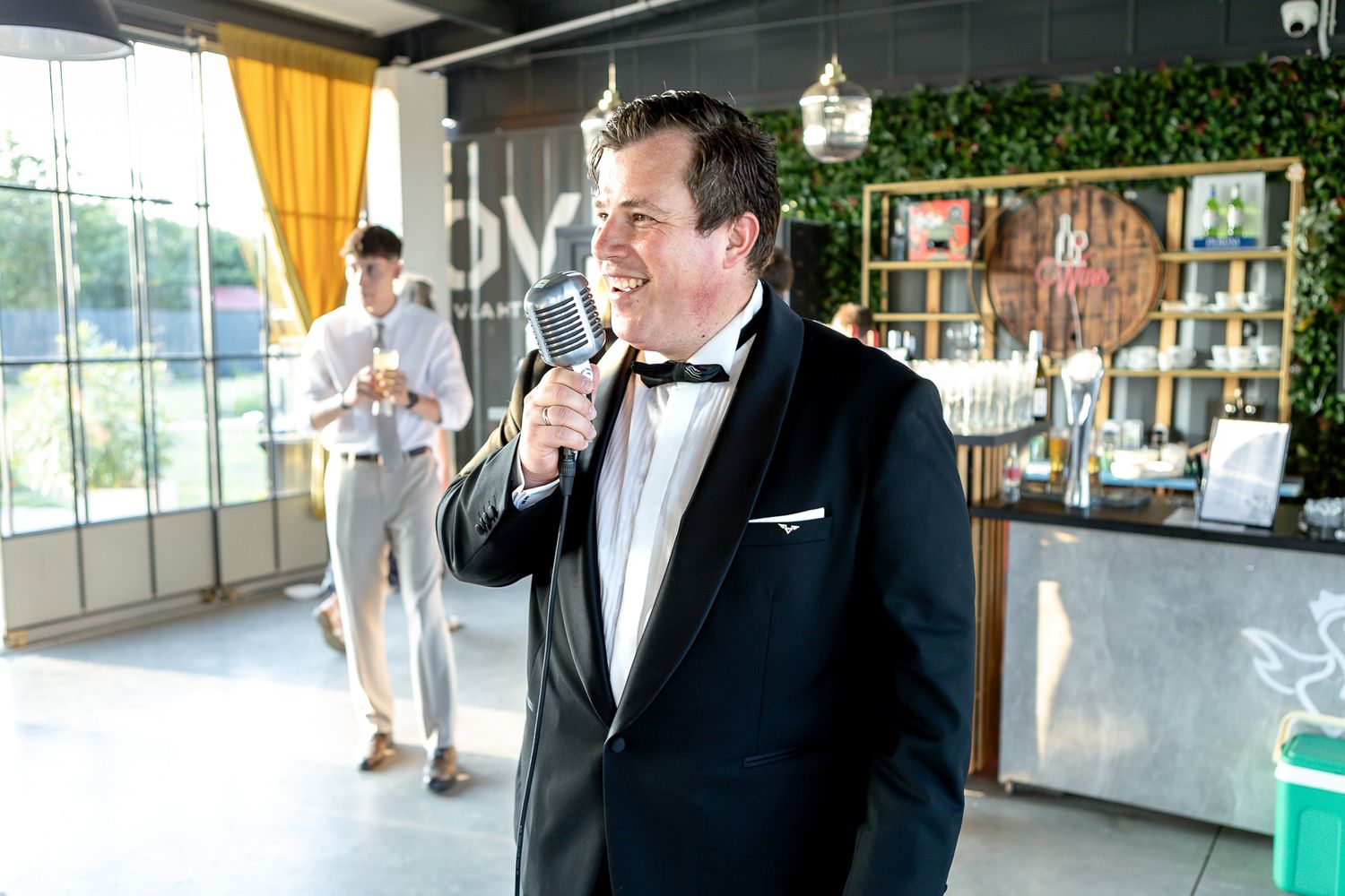 Wedding guests in white attire mingle and socialize during an indoor reception with elegant chandeliers.