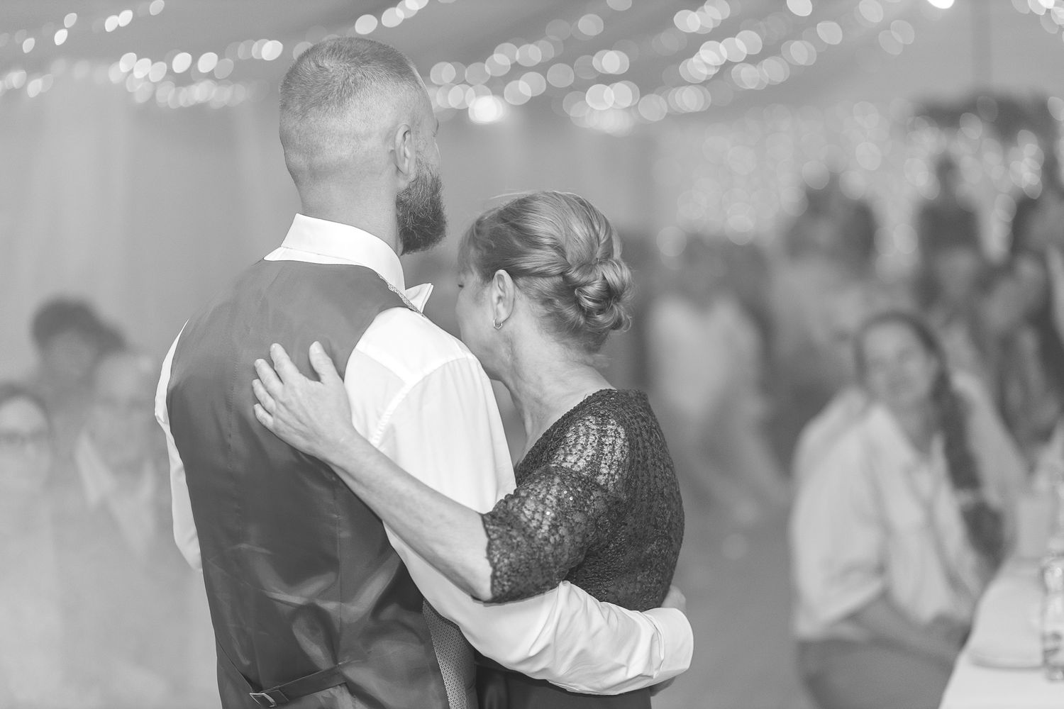 A group of people dance and celebrate at a wedding reception in black and white.
